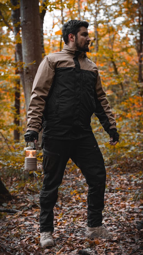 Man Standing in an Autumn Forest with a Lantern in Hand