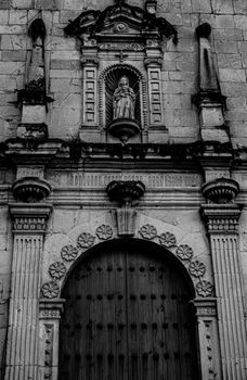Black and white photo of Santo Domingo Church facade, featuring architectural details and a religious statue in Oaxaca, Mexico.
