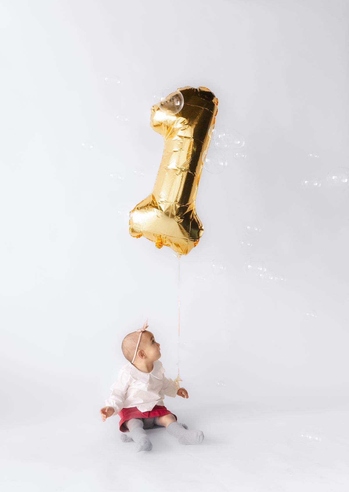 Baby sitting beside a large gold number one balloon kept at a safe distance