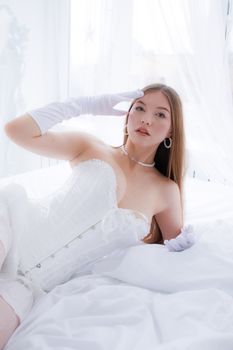 Stylish fashion portrait of a woman in bed wearing white lingerie and gloves, exuding elegance.