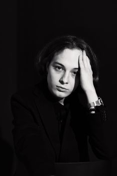 Young model in a black blazer posing thoughtfully in a dark studio setting.