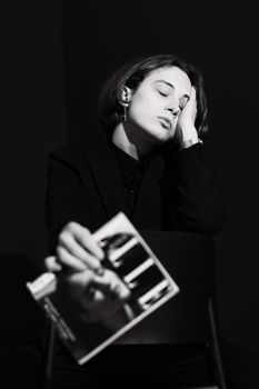 A moody black and white studio portrait of a woman posing with a magazine, reflecting elegance and modern fashion.
