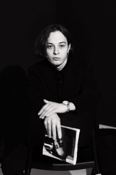 Black and white portrait of a woman with short hair holding a book against a dark background.