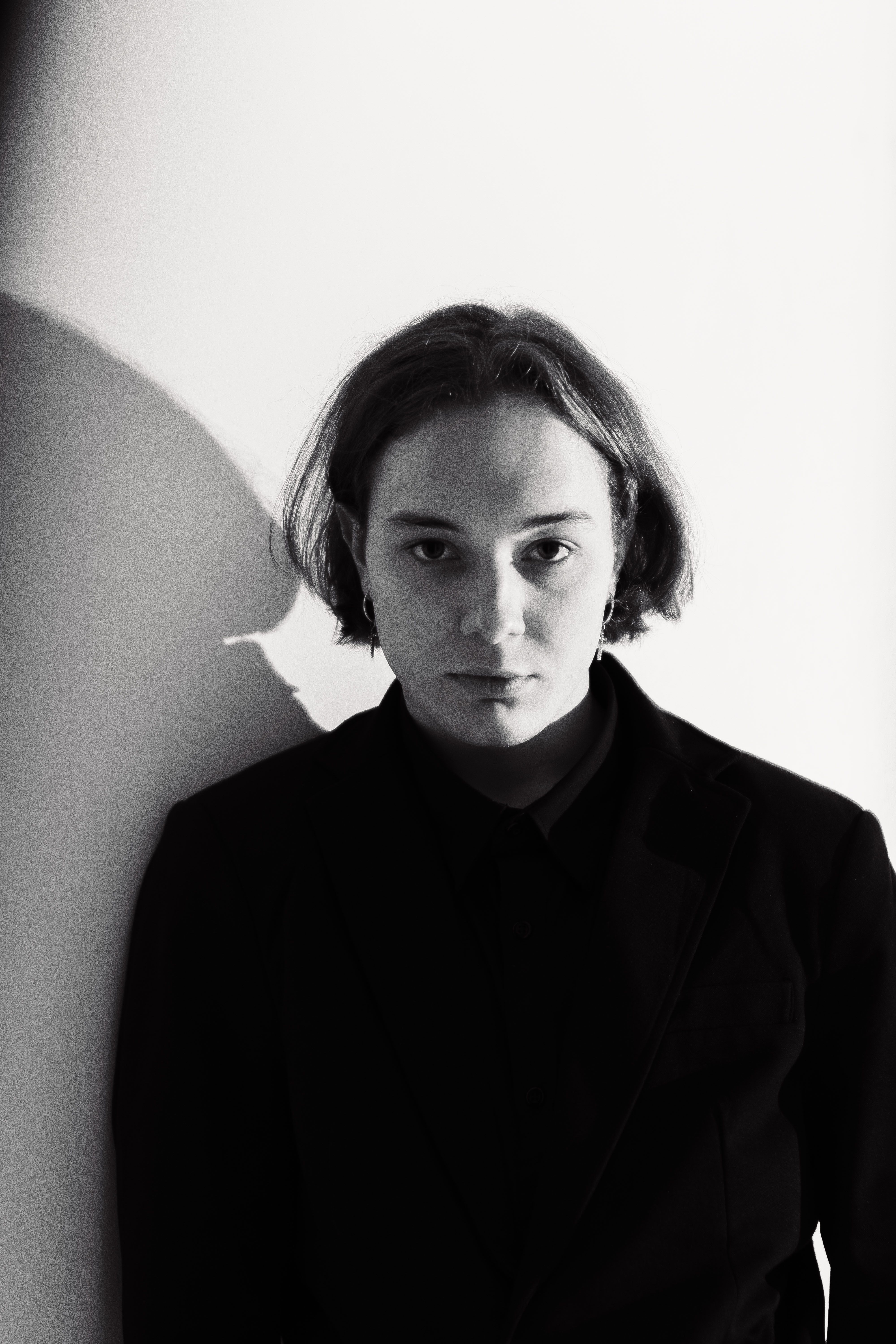 Black and white portrait of an adult in a blazer with dramatic shadows.