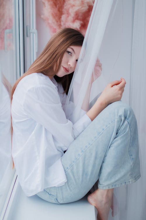 Free Woman in White Shirt and Jeans Sitting on Windowsill Stock Photo