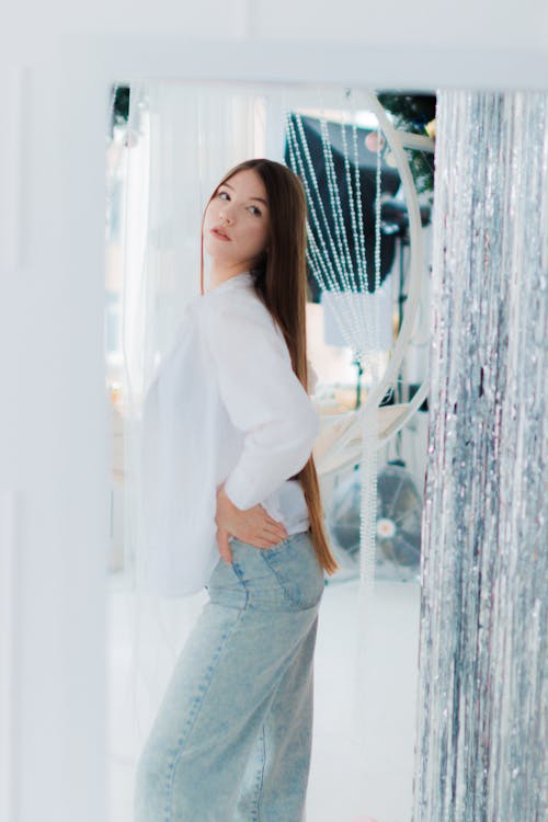 Young Woman in Jeans and Shirt Standing in front of a Mirror 