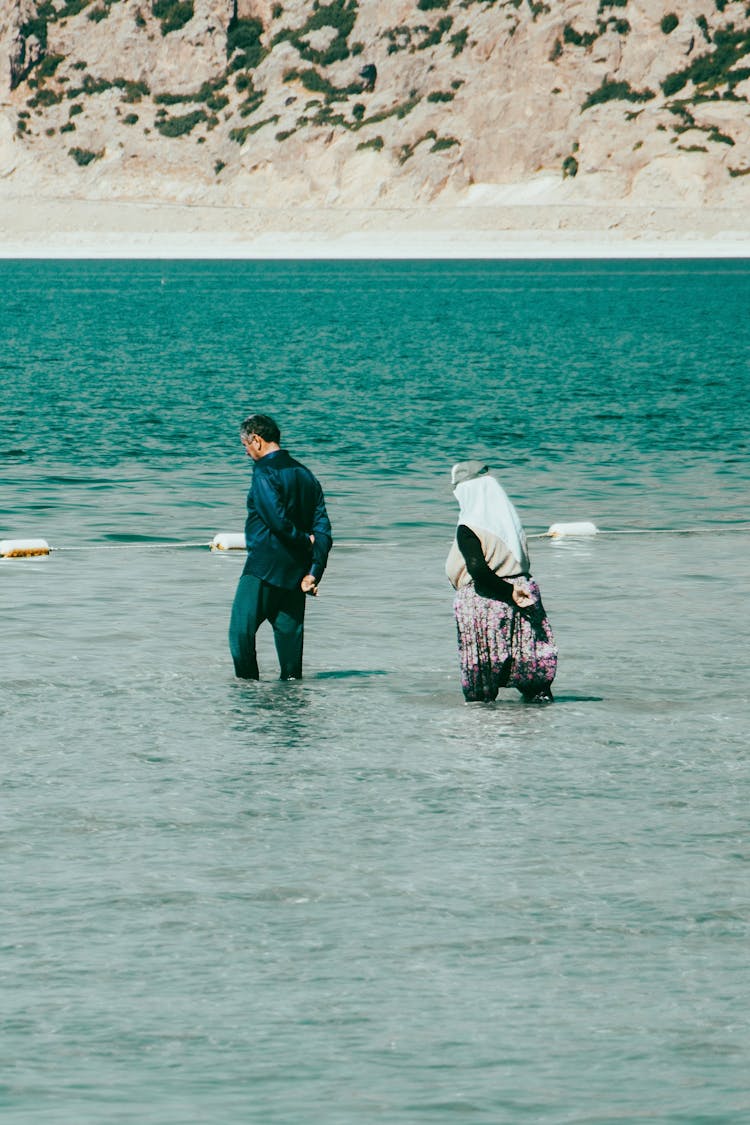 Man And Woman In Hjab Walking In Shallow Water On Sea Shore