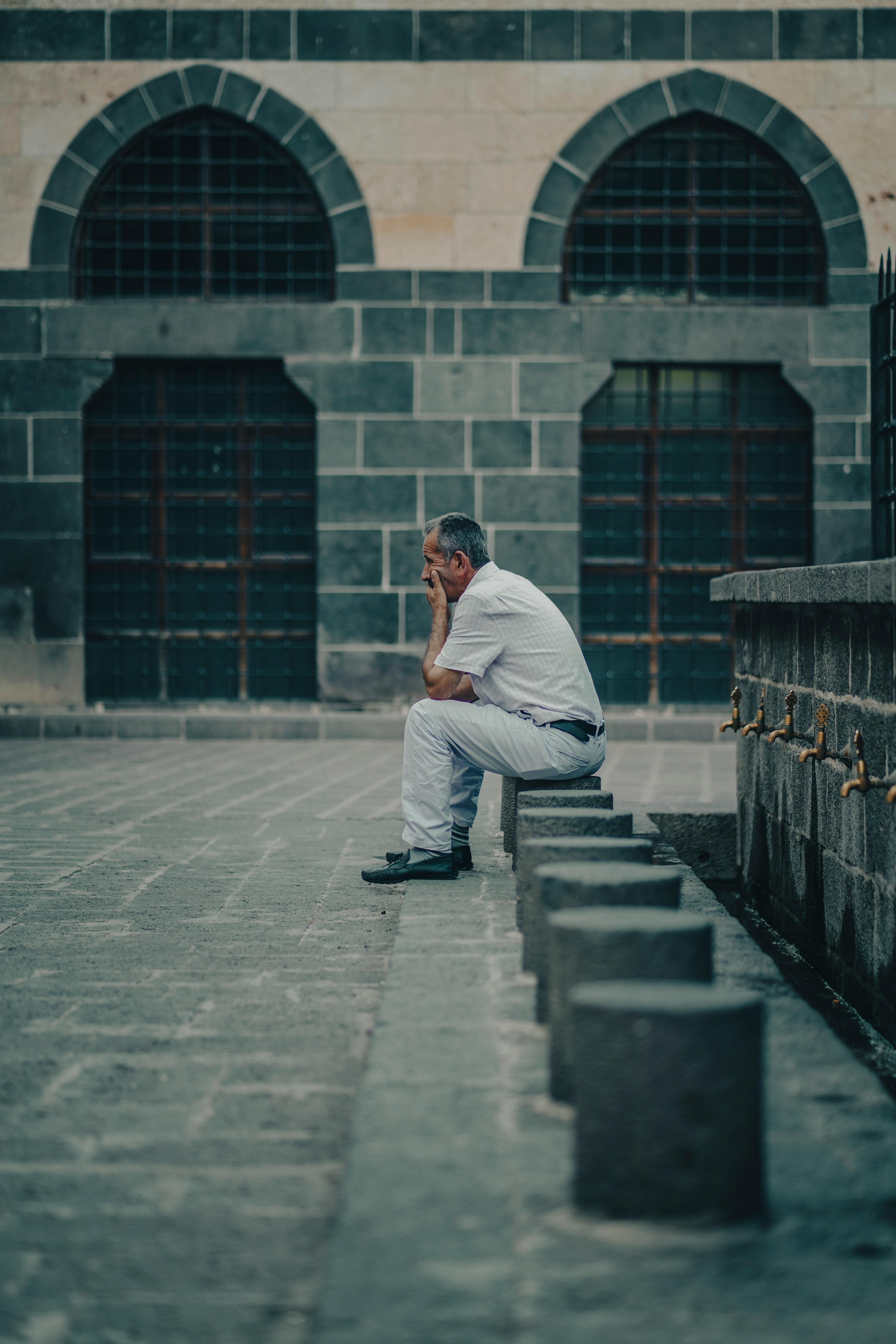 Man sits in deep thought outside a historic mosque in Türkiye, reflecting tranquility and culture.