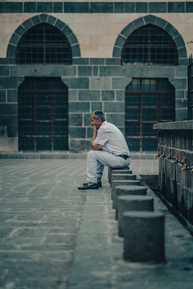 Candid Photo Of A Man Sitting In Front Of A Mosque 