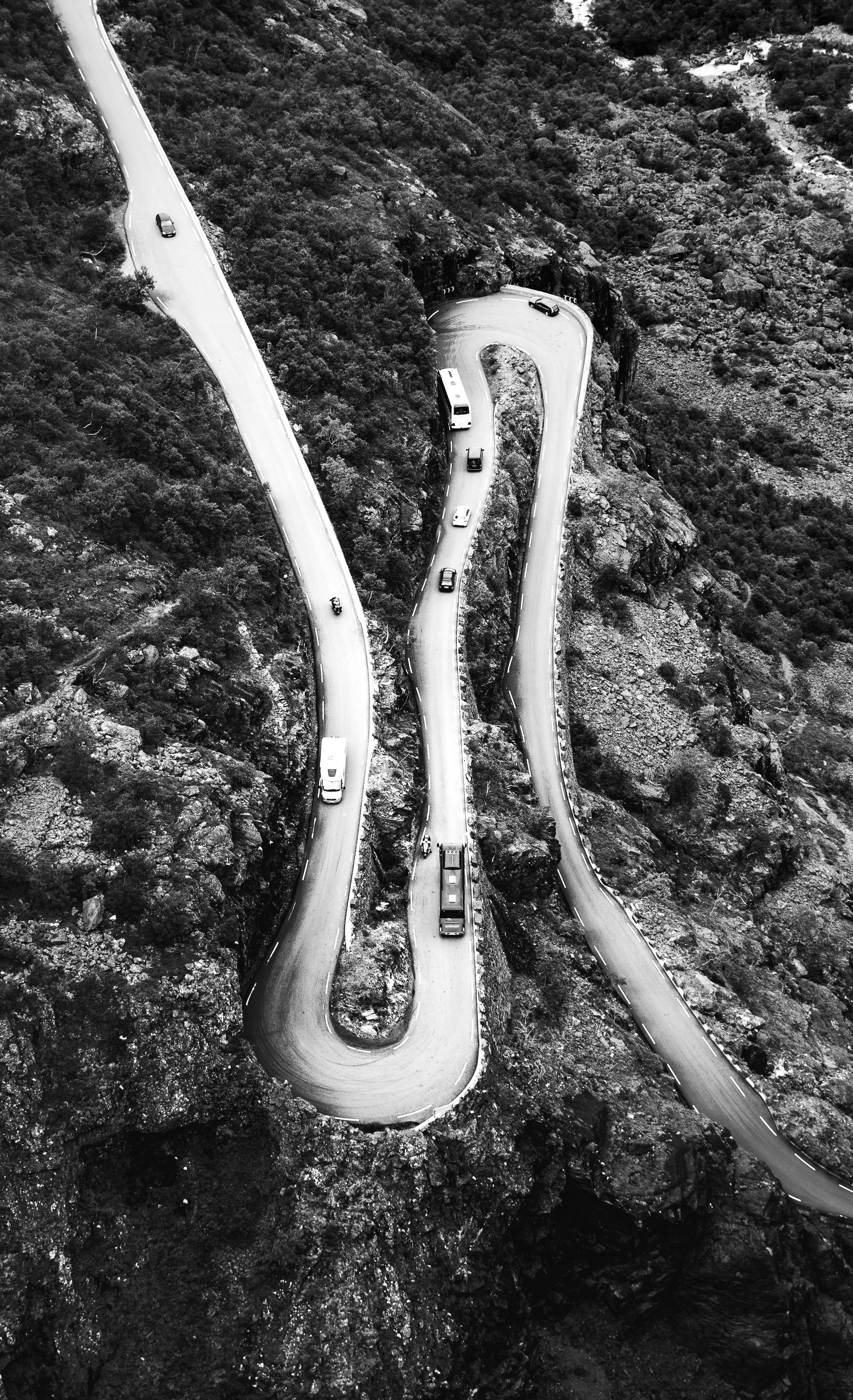 Black and white aerial shot of cars navigating a winding mountain road.