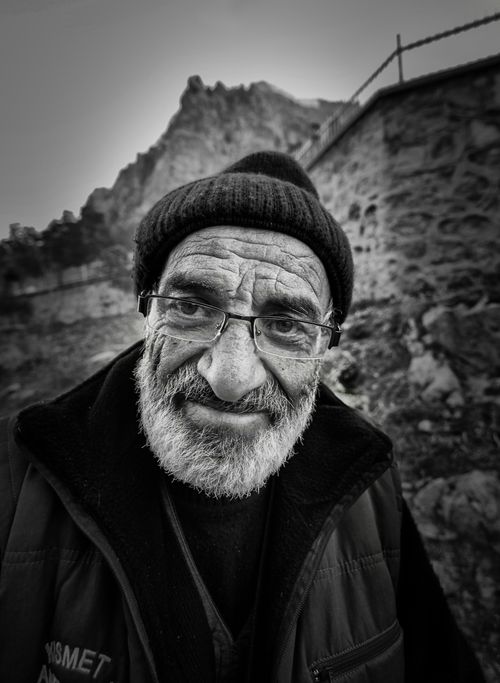 Free Black and white portrait of a bearded senior man wearing glasses and a hat, smiling outdoors. Stock Photo
