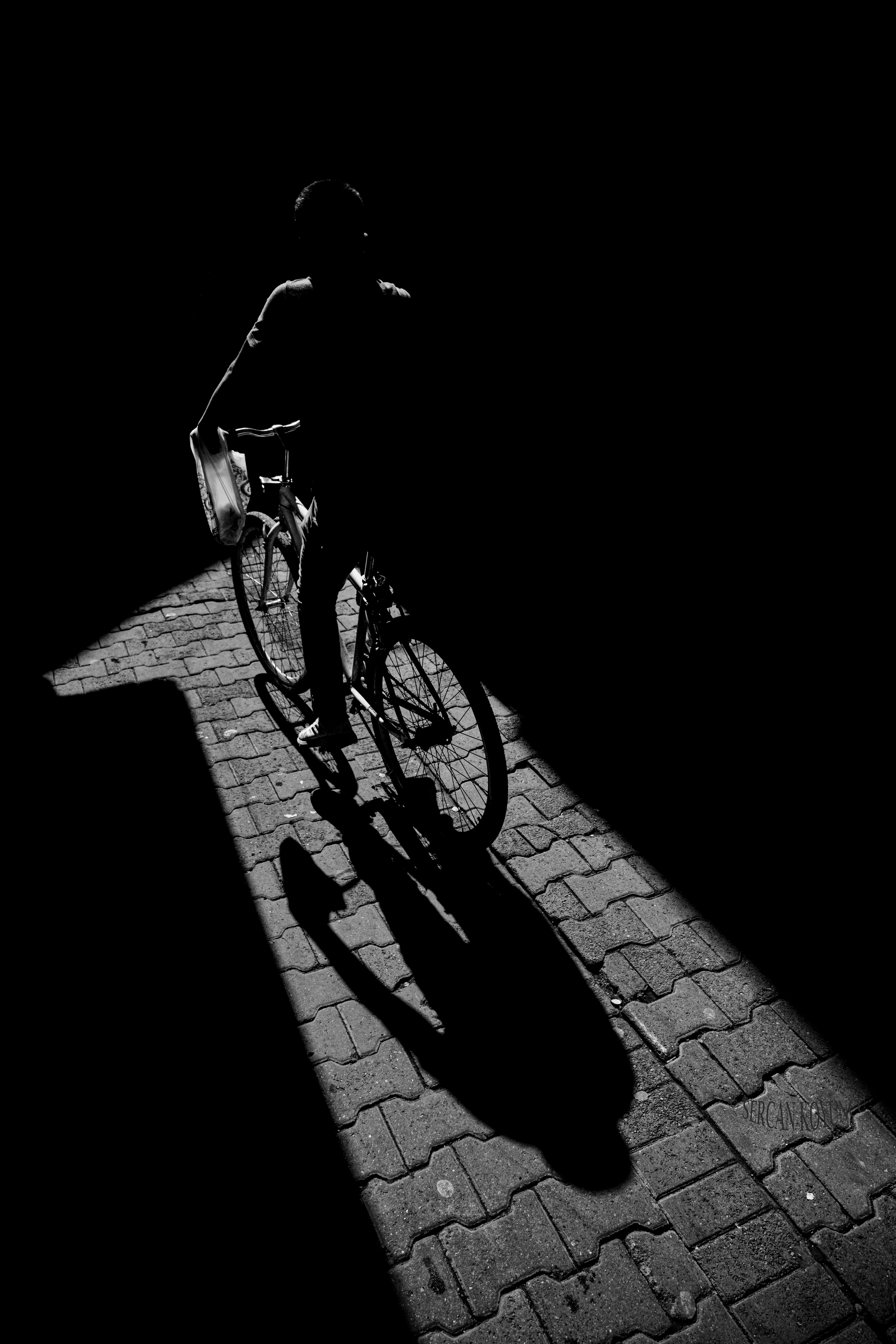 Dramatic black and white silhouette of a cyclist casting a shadow on urban pavement.