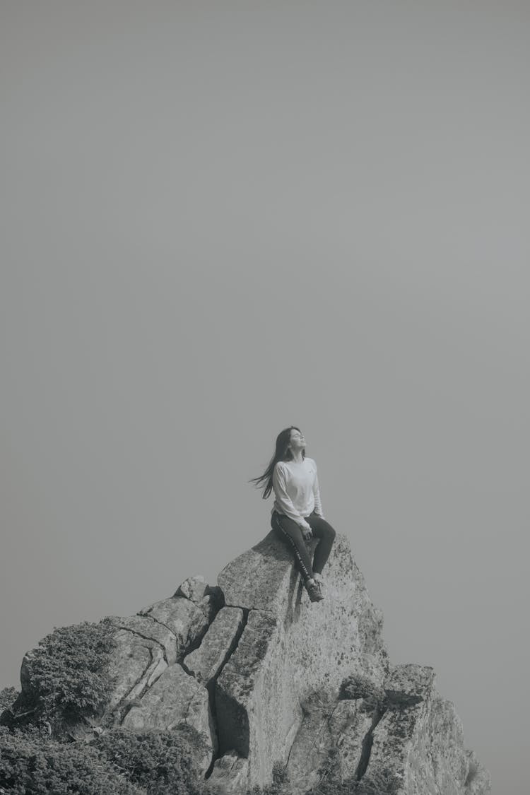 Woman Sitting At The Top Of A Rocky Mountain 