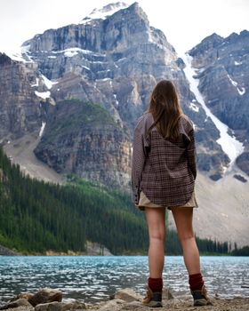 A woman stands admiring the scenic beauty of Moraine Lake and the Rocky Mountains in Banff, Canada.
