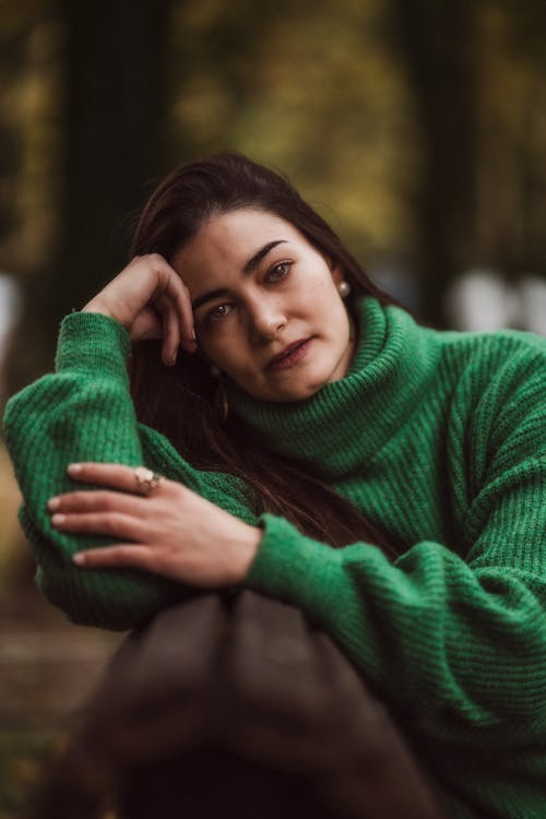 Young Woman in a Green Sweater Sitting on a Bench in a Park 