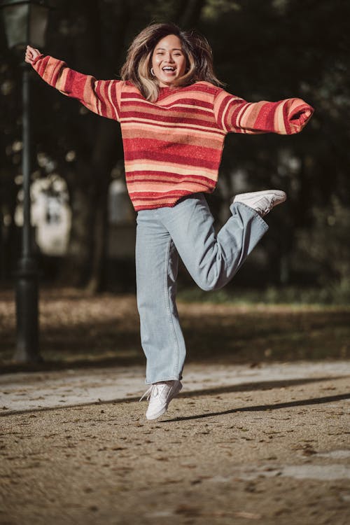 Young Happy Woman in a Sweater and Jeans Jumping in a Park 