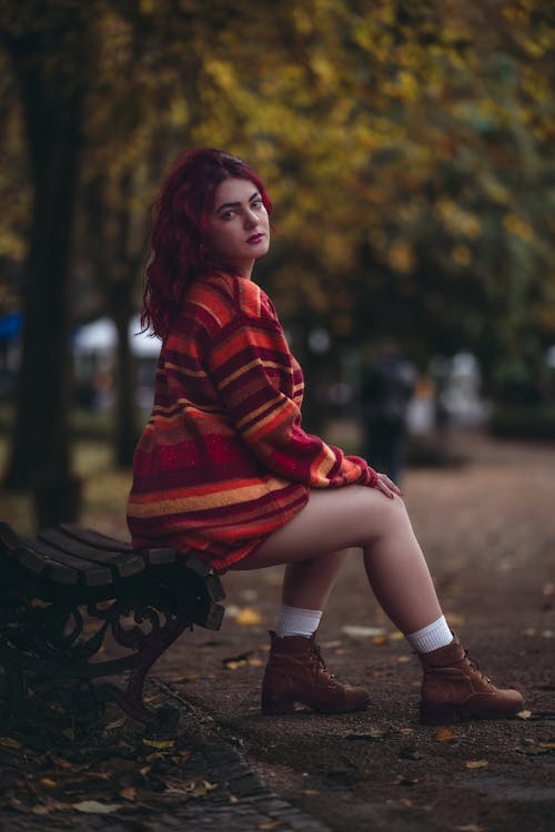Young Woman in a Striped Sweater Sitting on a Bench in a Park in Autumn