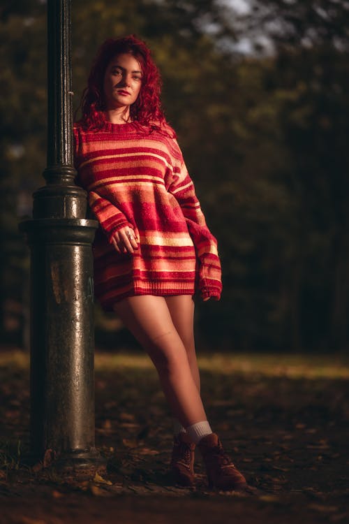 Young Woman in a Striped Sweater Standing by a Lamppost in a Park 