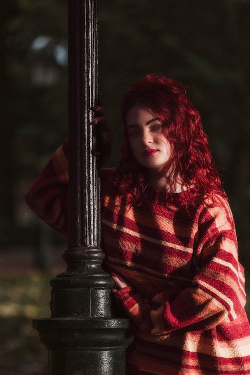 Young Woman in a Striped Sweater Standing by a Lamppost in a Park 