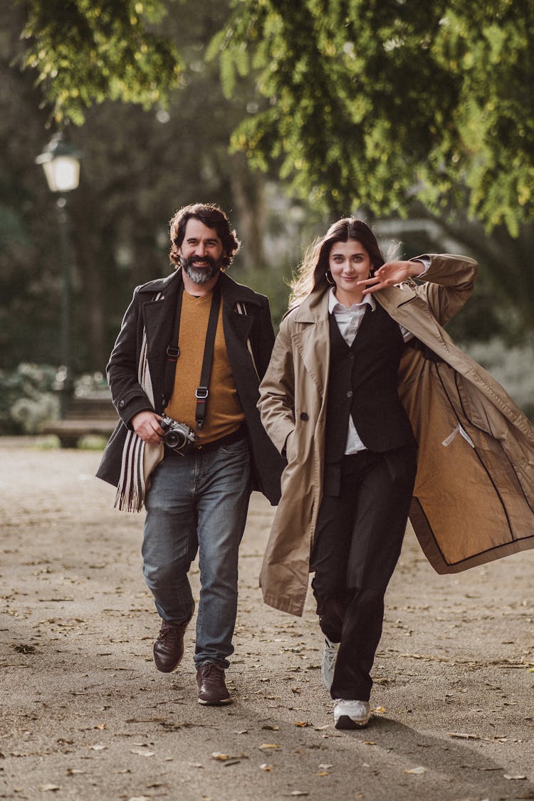 A Man And Woman Walking In A Park And Smiling 