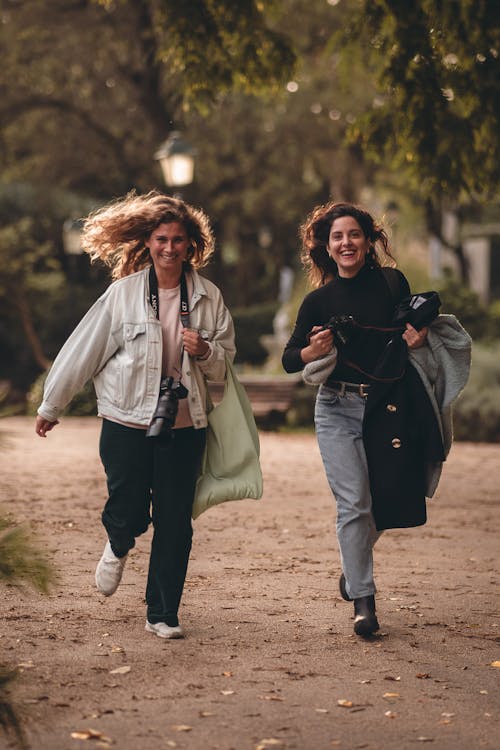 Two Women with Cameras Walking in a Park and Smiling 