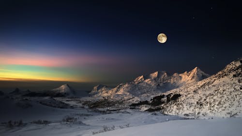Scenic View of Snowy Mountains on the Shore under a Sunset Sky with Full Moon