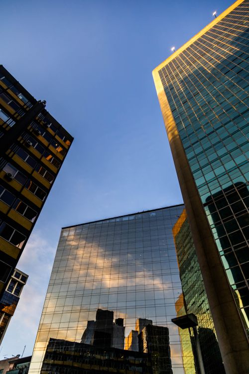 Free Upward view of modern skyscrapers with reflective glass facades capturing a cloudy sky. Stock Photo