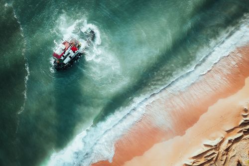 Free Aerial view of a shipwreck near the sandy shores of Chukai, Malaysia, showcasing vibrant ocean waves. Stock Photo