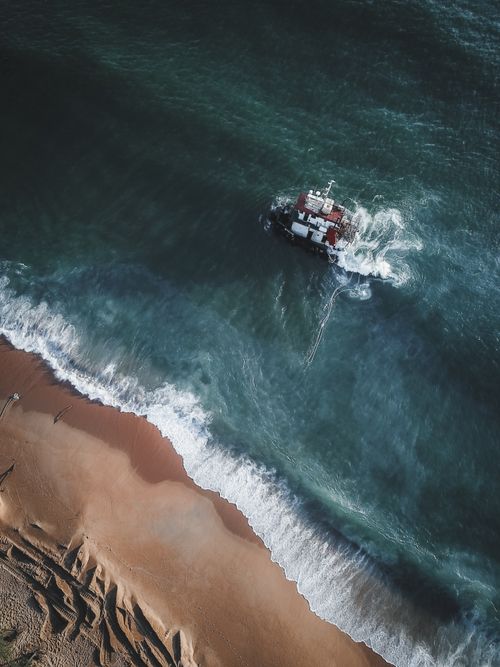 Free Drone shot of a shipwrecked vessel near the Chukai coastline in Malaysia with waves crashing onto the shore. Stock Photo