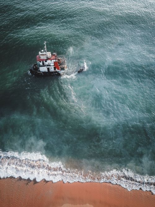 Free Aerial shot of a fishing boat near Chukai, Malaysia, with waves meeting the shore. Stock Photo