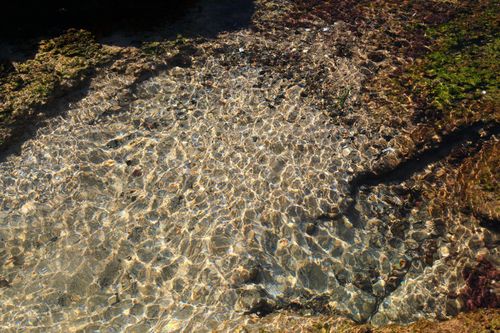 Free A serene view of sunlight reflecting on clear water over rocks, showcasing nature's beauty. Stock Photo