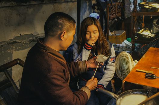 Chinese sugar-blowing artist and young girl in a Chengdu workshop creating sugar sculptures.