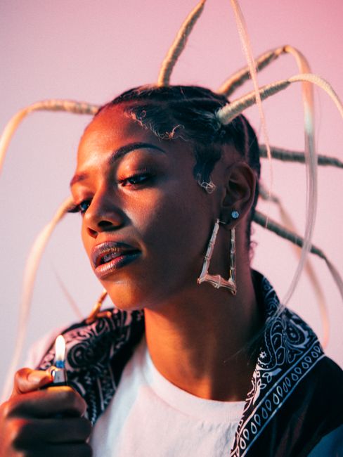 Vibrant portrait of a stylish woman with creative hairstyle and big earrings, holding a lighter.