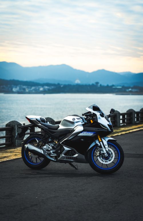 Free A sleek modern motorcycle parked on a lakeside road with mountains in the background. Stock Photo