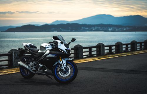 Free A sleek sports motorcycle parked by a scenic waterfront during sunset, mountains in the background. Stock Photo