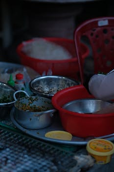 Close-up of street food preparation featuring various cooking utensils and ingredients on a tray.
