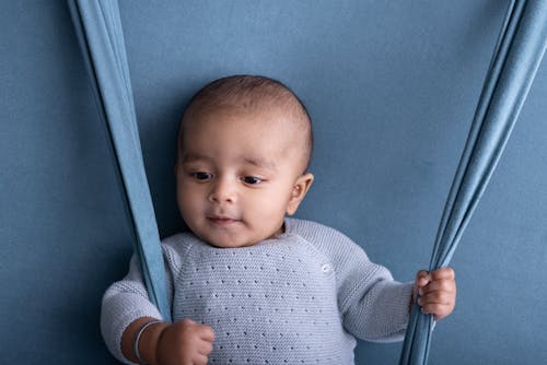 A baby is sitting on a swing with blue fabric