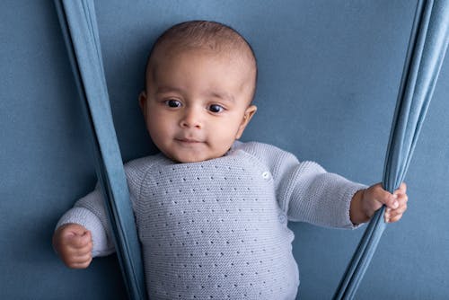 A baby is sitting on a blue background with a blue sweater