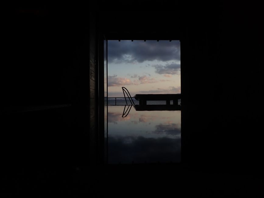 Silhouetted poolside scene reflecting sky at sunset.