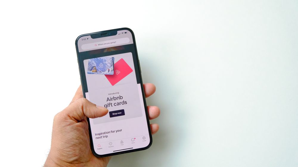 Close-up of a hand holding a smartphone displaying Airbnb gift cards on a white background.