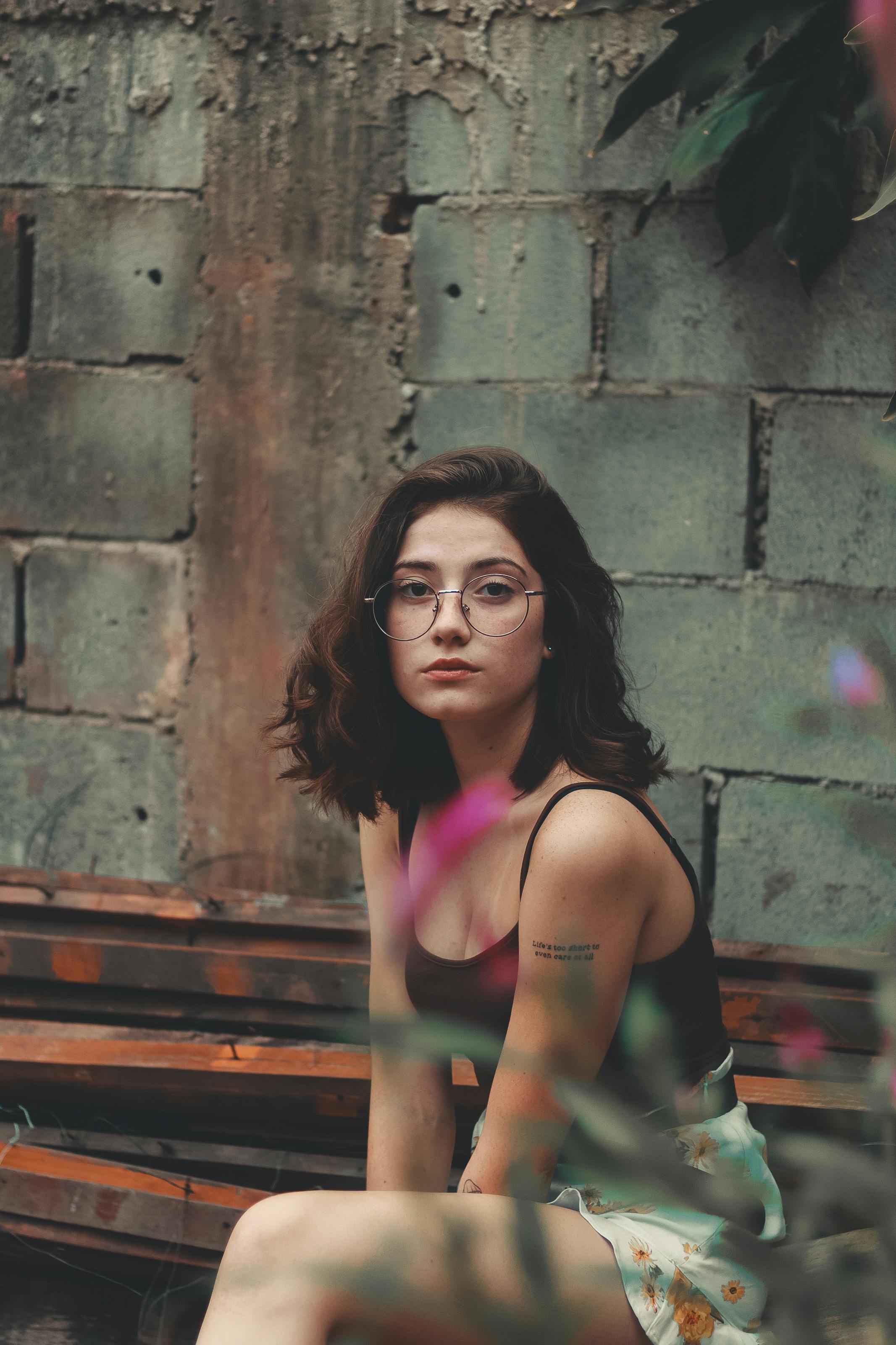 一位年轻女子戴着眼镜，身着休闲服装，坐在后院纹理墙前