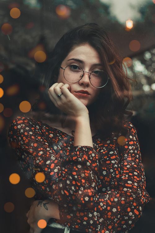 Free Portrait of a contemplative woman wearing glasses and a floral dress with bokeh lighting effect. Stock Photo