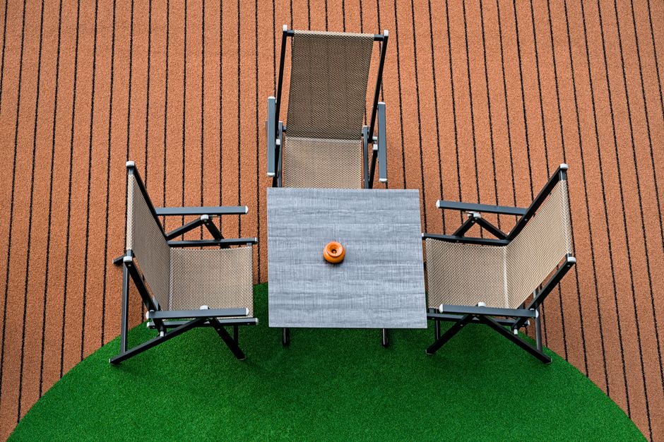 Four empty mesh chairs around a table on a striped terrace, captured from above.