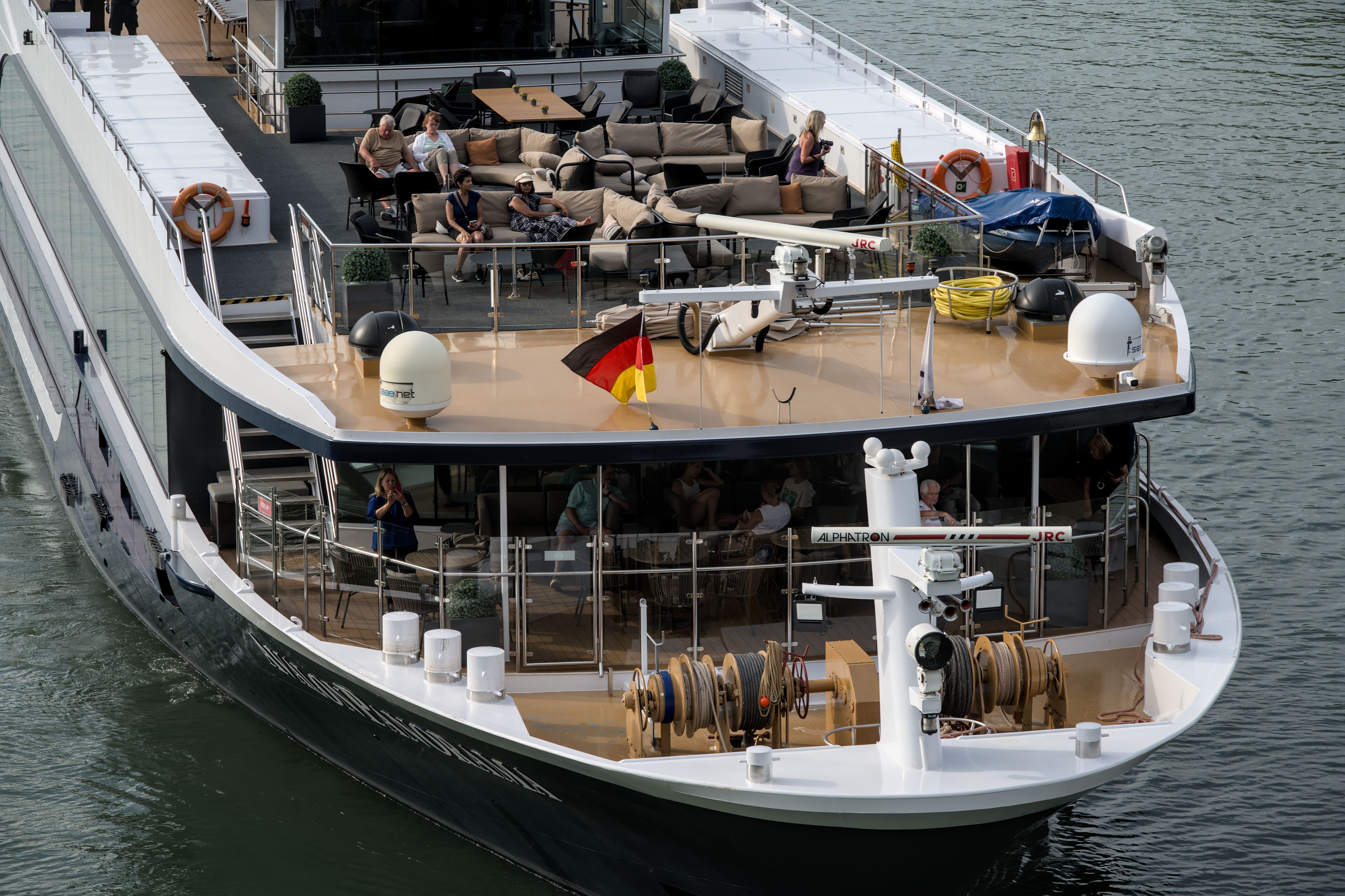 River cruise ship with passengers relaxing on the open upper deck beneath a German flag