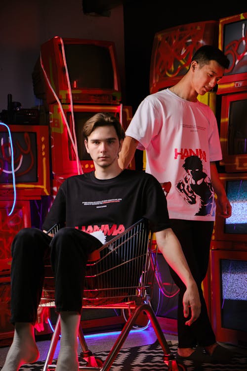 Two Young Men Posing among Old TVs and Sitting in a Shopping Cart 