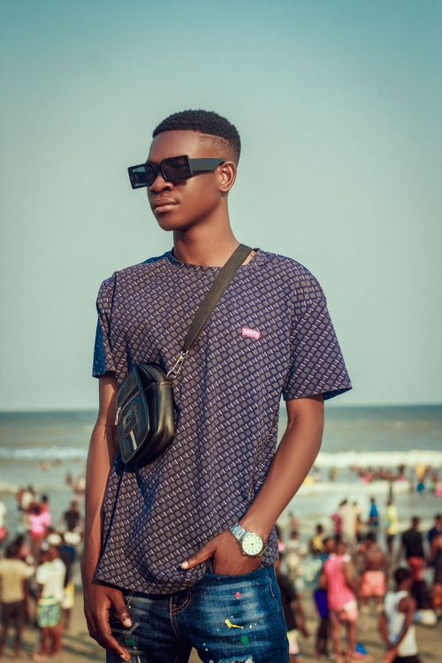 Free Fashionable young man in sunglasses poses confidently at a crowded beach under a clear sky. Stock Photo
