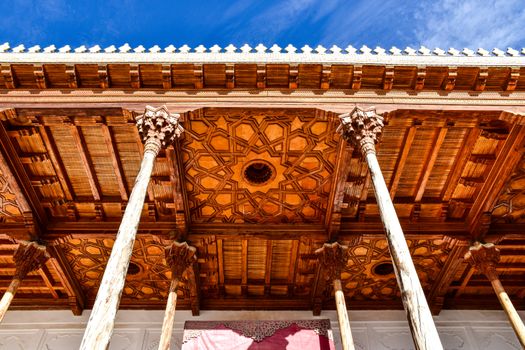Detailed view of a beautifully ornamented wooden ceiling supported by columns outdoors in Uzbekistan.