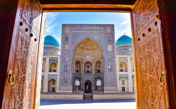 Stunning view of an ornate Uzbek madrasah with blue domes through a carved doorway.