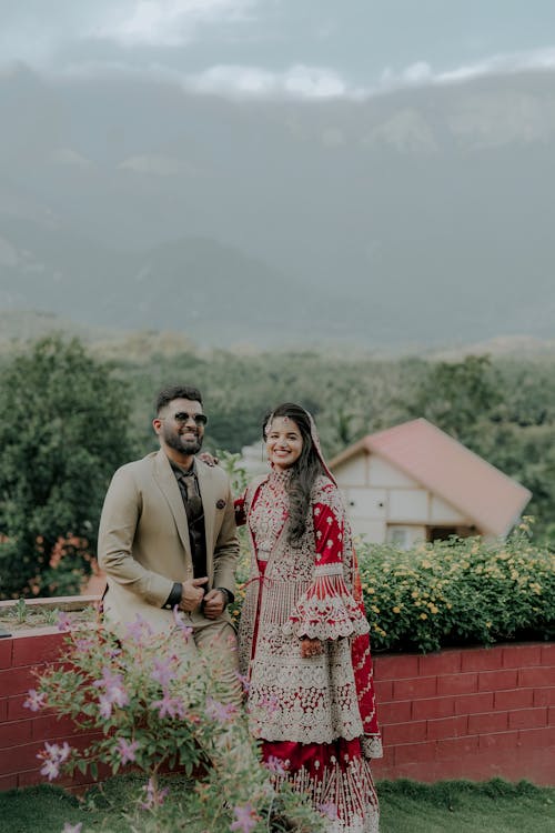 Smiling Newlyweds Standing Together by Wall with Flowers