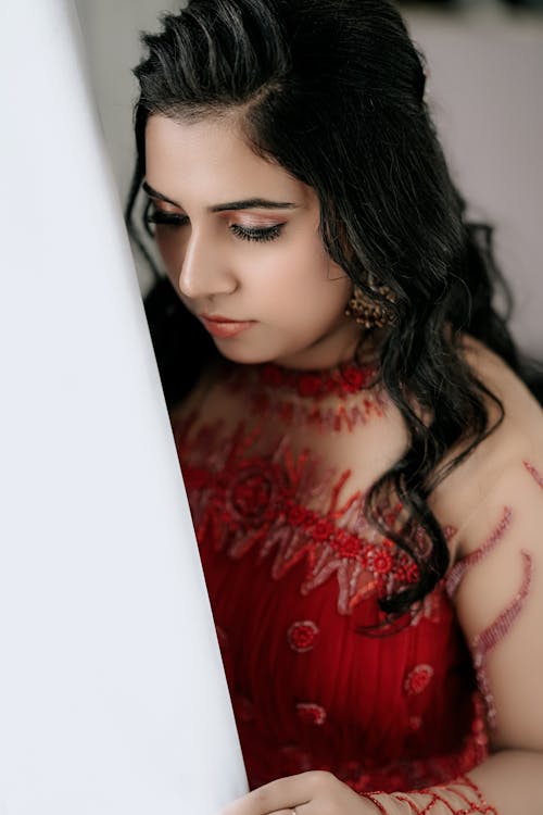 Young Woman in a Embroidered Red Dress with Long Beige Sleeves by Curtain